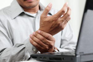Man holding his wrist in pain, in front of a laptop computer